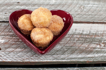 Side view of a heart shaped bowl filled with mini French breakfast puffs on a weathered barn wood table