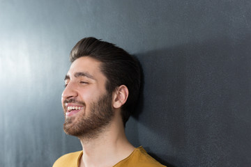 sexy man with beard smiling big against wall
