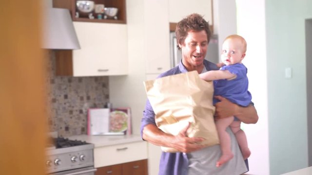 Modern Dad Unpacking Groceries with Infant Girl In Arms