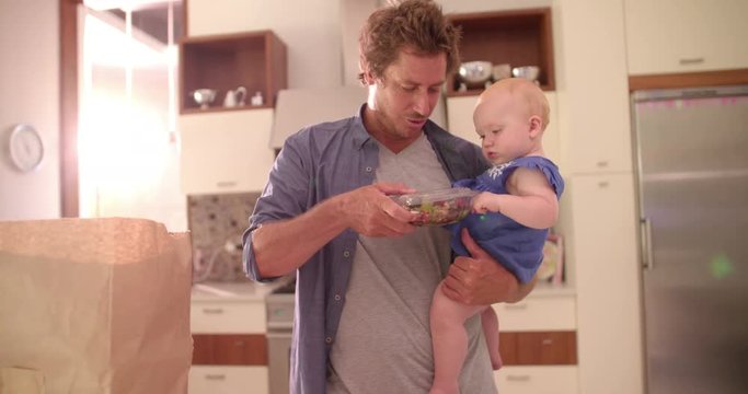 Modern Dad Unpacking Groceries with Infant Girl In Arms