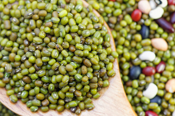Mung beans in wooden spoon with mixed beans in rattan tray in the background