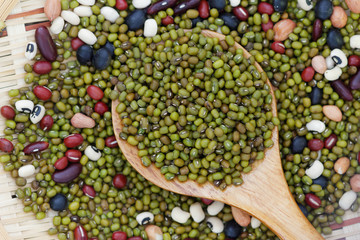 Mung beans in wooden spoon with mixed beans in rattan tray in the background