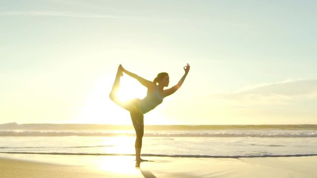 Happy young woman practicing yoga on the beach at sunset. Healthy active lifestyle concept. Slow Motion