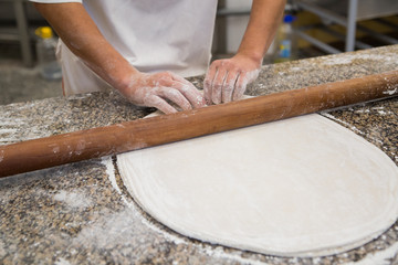 Hands baking dough with rolling pin on wooden table