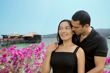 Happy interracial couple in love at sea side with bungalow backg