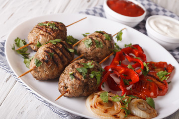 Kofta kebab with grilled vegetables on a plate and sauce close-up. Horizontal
