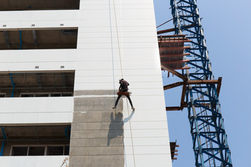 Worker painting high rise building in construction site.High risk working concept.