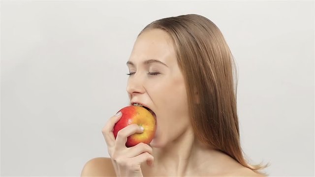 Blonde girl with braces eating apple. White. Closeup. Slow motion