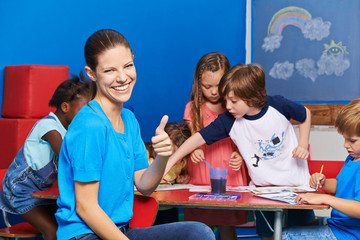 Kindergärtnerin mit Gruppe Kinder hält Daumen hoch