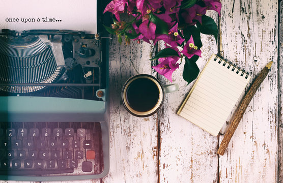 image of vintage typewriter with phrase "once upon a time", blank notebook, cup of coffee on wooden table

