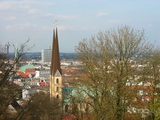 Blick durch die Bäume auf die City von Bielefeld mit der Neustädter Marienkirche bei Sonnenschein im Frühling am Hermannsweg im Teutoburger Wald in Ostwestfalen-Lippe