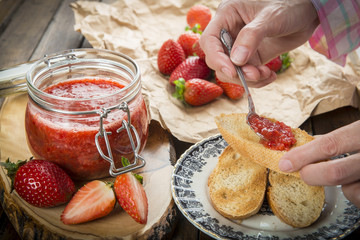 Manos untando mermelada de fresa casera en una tostada de pan para el desayuno