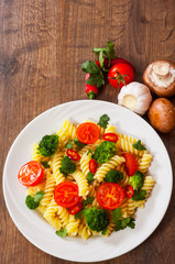 Fusilli pasta with cherry tomatoes and broccoli in a plate on wooden table