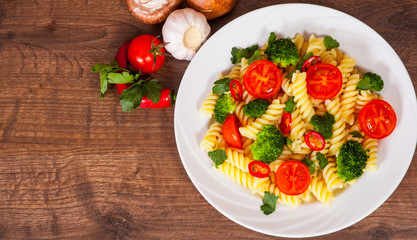 Fusilli pasta with cherry tomatoes and broccoli in a plate on wooden table
