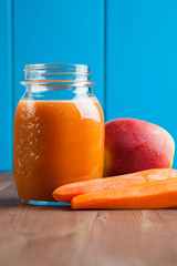 Healthy carrot apple smoothie in a jar on blue wooden background