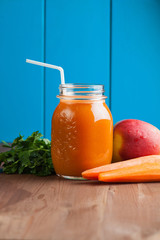 Healthy carrot apple smoothie in a jar on blue wooden background