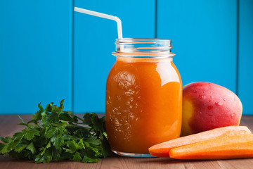 Healthy carrot apple smoothie in a jar on blue wooden background