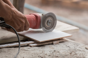 construction worker cutting a tile using an angle grinder - obrazy, fototapety, plakaty