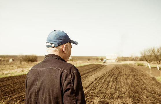 senior farmer looking at tractor plowing soil