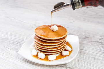Tasty pancake on a white plate, wooden background, maple syrup