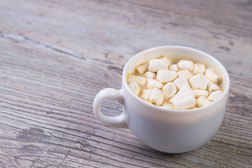 white Cup of hot cocoa with marshmallows on a light wooden background