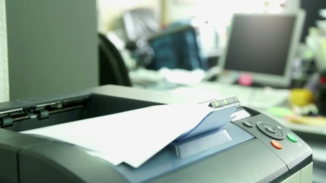 Printing document paper with laser printer. Office work and furnishings, stationery around in the background is seen the monitor