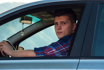 Young adult sitting in his car and looking to camera throught wi