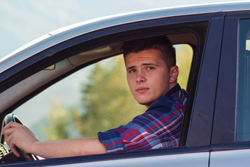 Young adult sitting in his car and looking to camera throught wi