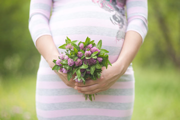 Closeup shot of pregnant woman with pink clover bouquet on her belly dressed in striped pink and grey dress