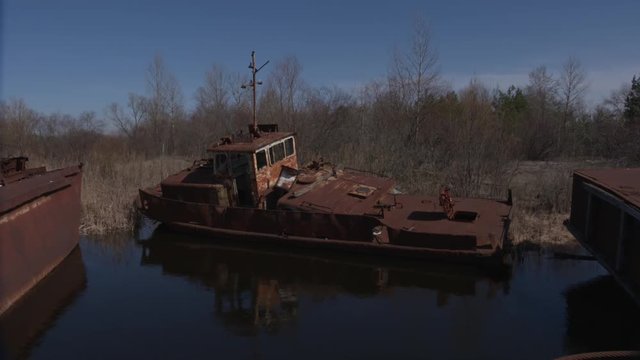Graveyard of ships on the river.  Many rusty barges and boats in water. Chernobyl zone of alienation