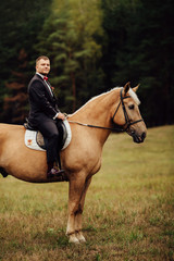 Obraz premium handsome groom sitting on brown horse in forest