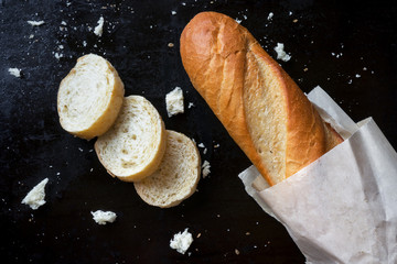 Sliced french baguette with crumbs on dark background
