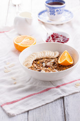 Homemade granola with fresh fruits in a white bowl with jam, milk and coffee on a wooden background for breakfast, closeup.