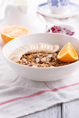 Homemade granola with fresh fruits in a white bowl with jam, milk and coffee on a wooden background for breakfast, closeup.