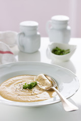 Vegetable cream soup with potatoes, carrot, mushrooms and cheese in a white plate on a white table, closeup, selective focus.