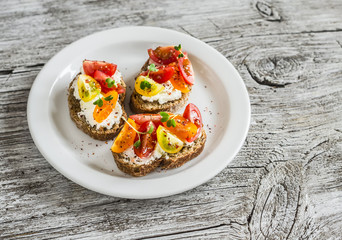 Tomato and cheese bruschetta on a white plate on rustic light wooden board. Healthy breakfast, snack or appetizer with wine