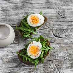 Sandwich with arugula and boiled egg on a wooden board. Healthy breakfast or snack