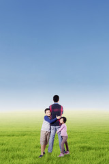 Naklejka na ściany i meble Two kids hugging their father at field