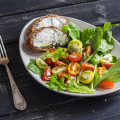 Fresh tomatoes and garden herbs salad and cheese sandwich on a white ceramic plate on dark wooden background. Delicious healthy food
