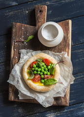 Puff pastry egg tartlet with fresh green peas and cherry tomatoes on wooden rustic board. Delicious breakfast or snack