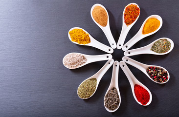 various spices in ceramic spoons on dark background