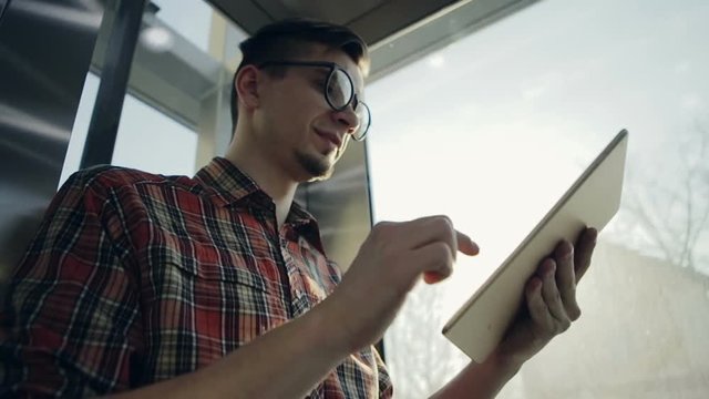 A young man lifting up by the elevator is becoming happy with his electronic device