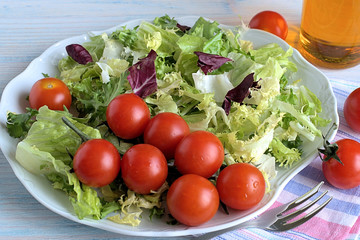Fresh lettuce and cherry tomatoes .   Leaves of fresh lettuce and cherry tomatoes on a white dish on a blue wooden background.