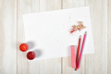 Top view of designer workplace equipped with red-pink gouache jars, colored pencils, chalk, shavings and white paper