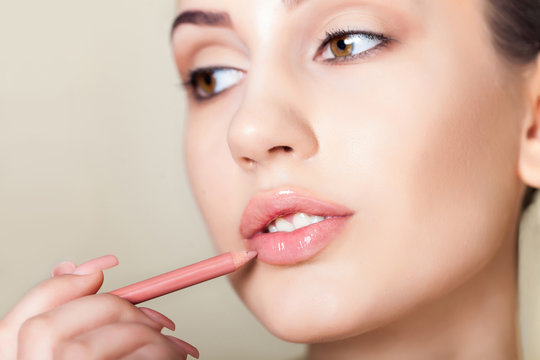 Sensual picture of woman face with makeup pencil on lips. Applying lips contour