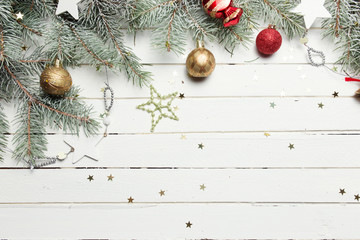 Fototapeta na wymiar Christmas or New Year decoration background: fur-tree branches, colorful glass balls and glittering stars on white wooden background, top view, copy space