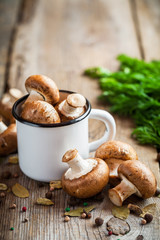 Mushrooms champignons in mug and spices on wooden table.