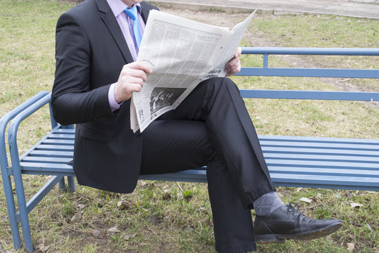 man reading a newspaper on a bench
