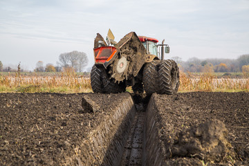 Tractor with double wheeled ditcher digging drainage canal