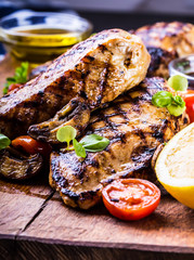 Grilled chicken breast in different variations with cherry tomatoes, .mushrooms, herbs, cut lemon on a wooden board or teflon pan. Traditional cuisine. Grill kitchen.